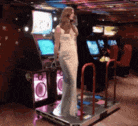 a woman in a white dress is standing on a dancing machine in an arcade .