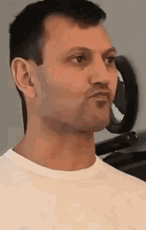 a man in a white t-shirt is standing in front of a mirror and making a funny face .
