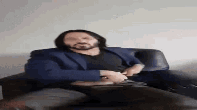 a man with a beard is sitting in a chair and adjusting his belt .