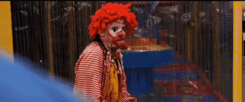 a man dressed as a clown with blood on his face is standing in the rain .