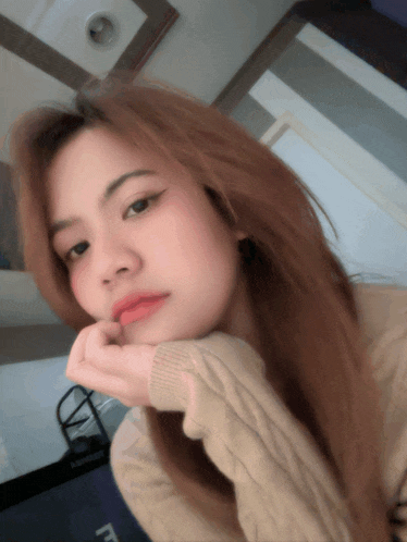 a woman is taking a selfie with her hand on her chin and the letter f is visible in the corner