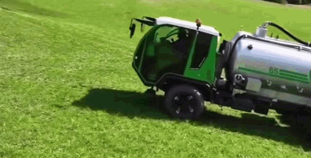 a green and silver truck is driving down a grassy hill