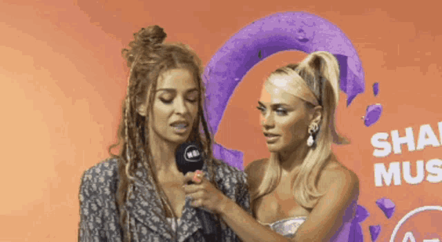 two women standing next to each other in front of a wall that says share music