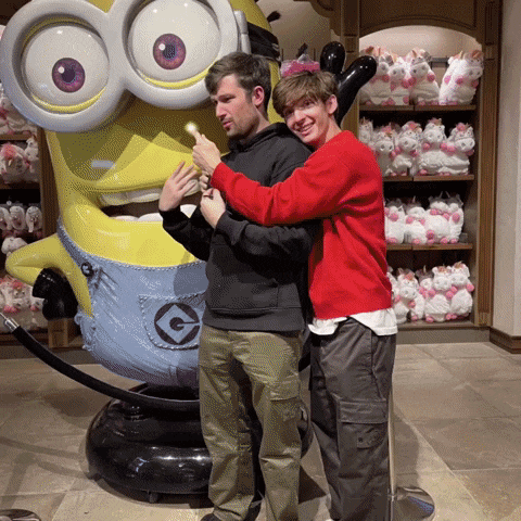 two men pose in front of a minion statue