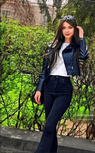 a woman wearing a blue jacket and jeans is standing in front of a fence