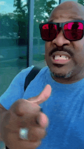 a man wearing red sunglasses and a blue shirt is pointing