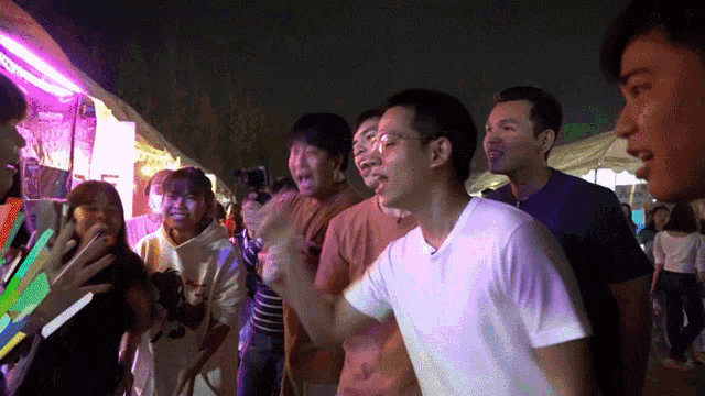 a man in a white shirt stands in a crowd of people at night