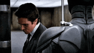 a man in a suit and tie stands next to a gray robot