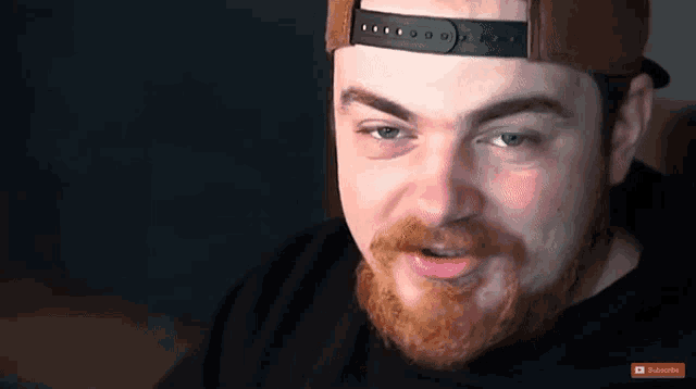 a man with a beard is wearing a hat and a black shirt with a subscribe button on the bottom