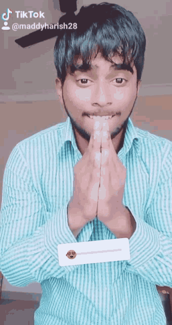 a man in a striped shirt has his hands folded in front of his face and says tiktok