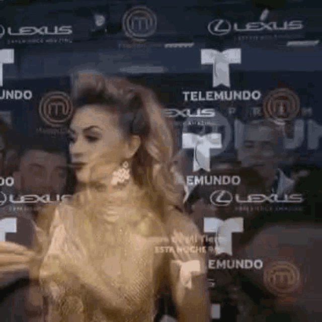 a woman in a gold dress is standing in front of a wall with logos for lexus .