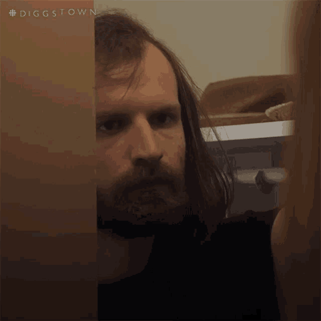 a man with long hair and a beard is peeking through a door with the hashtag #diggstown