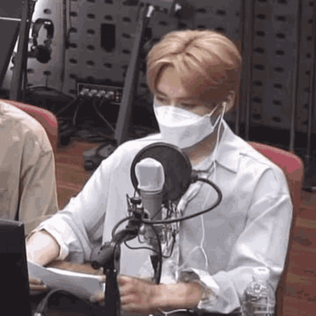 a man wearing a mask is sitting in front of a microphone in a room .