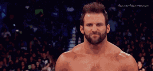 a shirtless wrestler with a beard is standing in front of a crowd of people .
