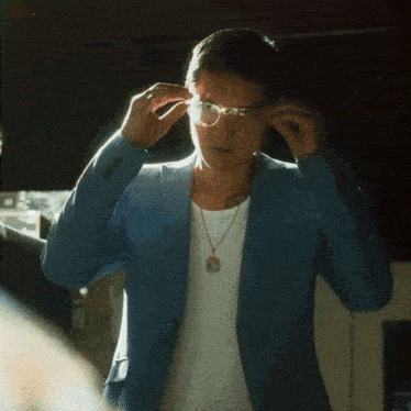 a man wearing a blue jacket and glasses is adjusting his glasses