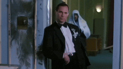 a man in a tuxedo is standing in a hallway with a ghost behind him