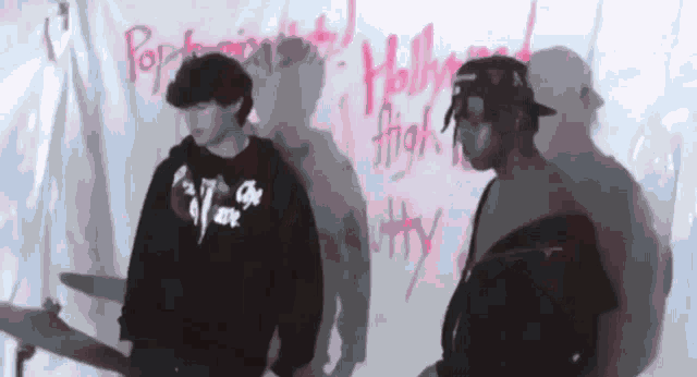 two men are standing in front of a wall that has the word hollywood written on it