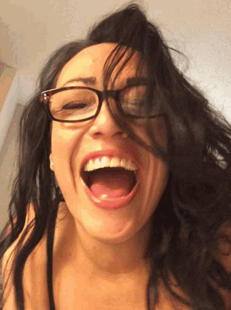 a woman wearing glasses laughs with her mouth open