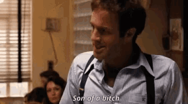 a man in a blue shirt and suspenders is talking to another man in a room .