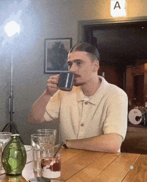 a man sits at a table drinking from a mug with the letter a in the background