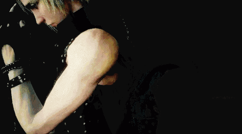 a man with blonde hair is wearing gloves and a black vest .