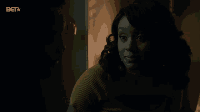 a woman in a yellow sweater is smiling in a dark room with a bet logo in the background