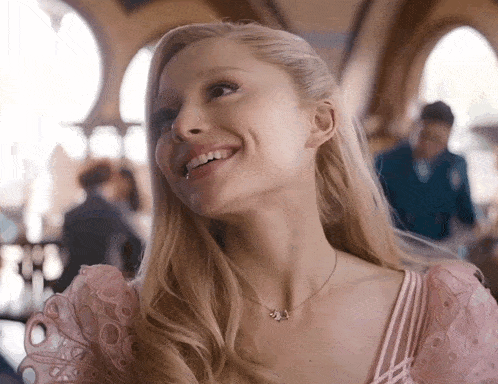 a woman in a pink dress is smiling and wearing a necklace with the letter j. on it