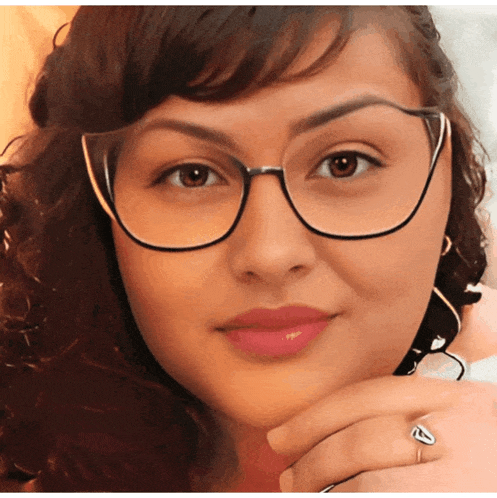a woman wearing glasses and a heart shaped ring looks at the camera