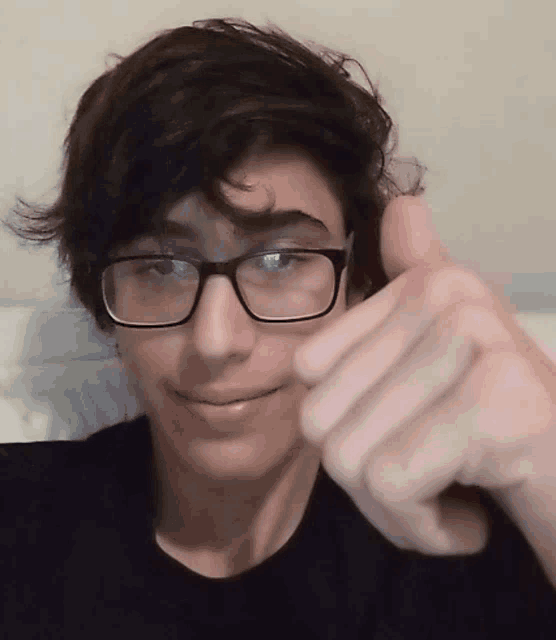 a young man wearing glasses is giving a thumbs up sign