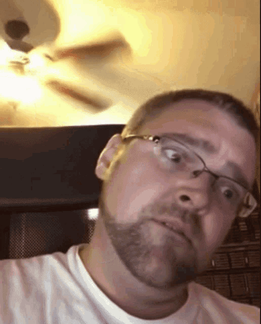 a man with glasses and a beard makes a funny face in front of a ceiling fan