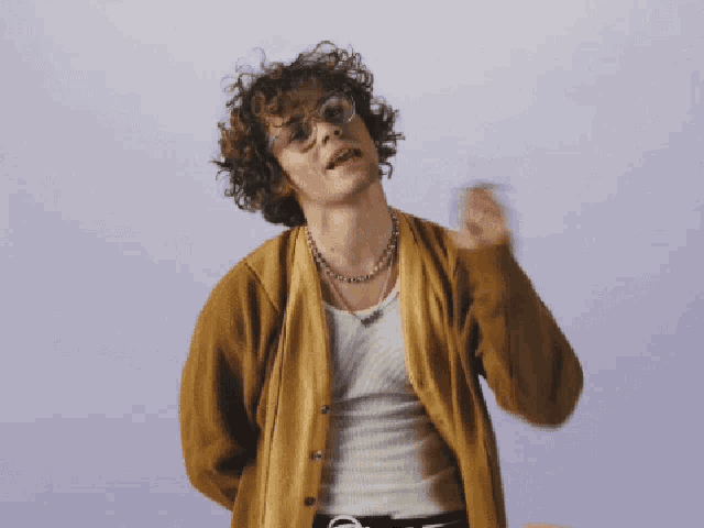 a man with curly hair wearing glasses and a cardigan