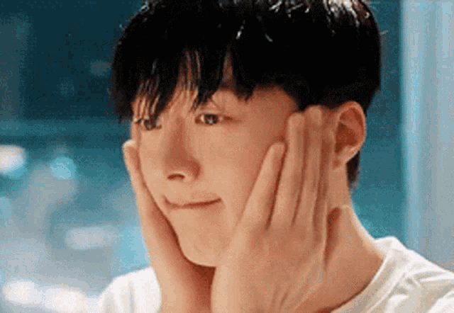 a young man is touching his face with his hands .