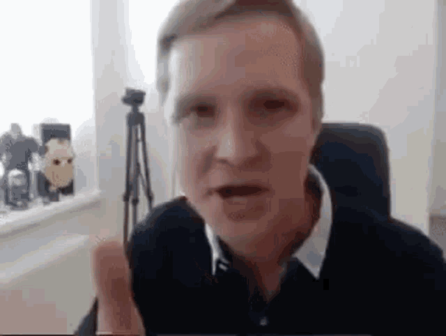a man is sitting in a chair and talking on a video call while pointing at the camera .