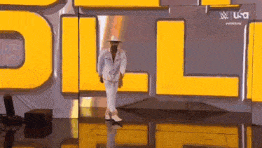 a man in a suit and hat is walking on a stage in front of a yellow sign .