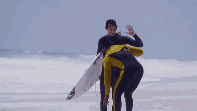 a man in a yellow wetsuit with the number 6 on his back is hugging another man
