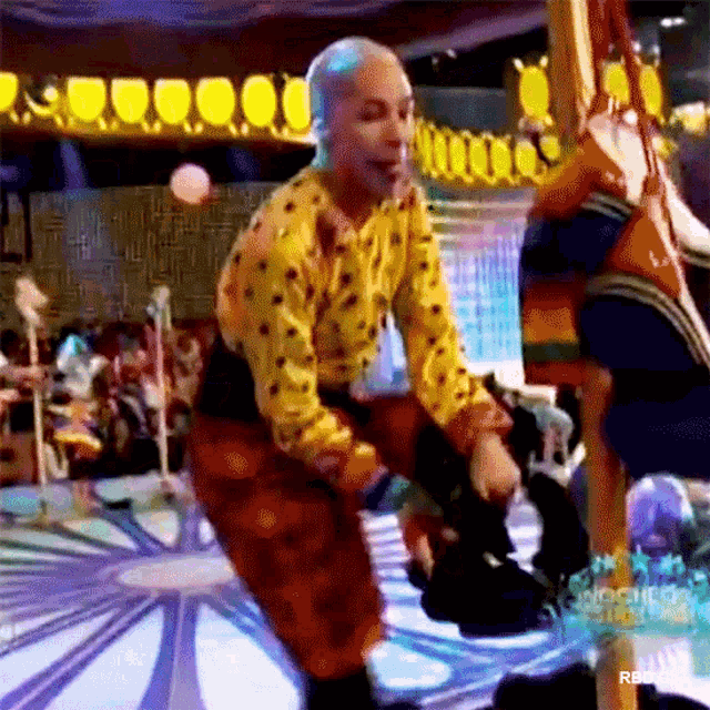 a bald man in a yellow shirt and orange pants is dancing