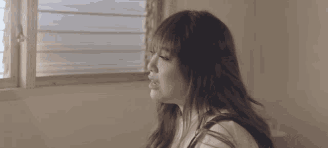 a woman with long hair looks out a window