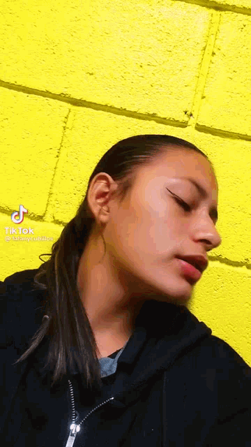 a girl is standing in front of a yellow brick wall and looking down .