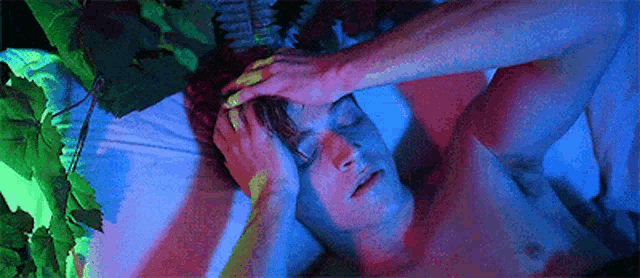 a shirtless man is laying on a bed with his eyes closed and holding his head .