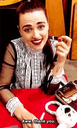 a woman with a tattoo on her wrist is sitting at a table with a stuffed animal and says aww thank you .