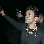 a woman in a black dress is holding a gun in her hand .