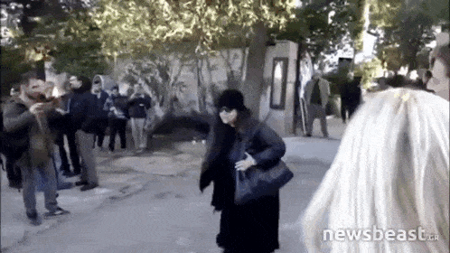a woman in a black coat stands in front of a group of people with the words newsbeast.gr on the bottom of the screen