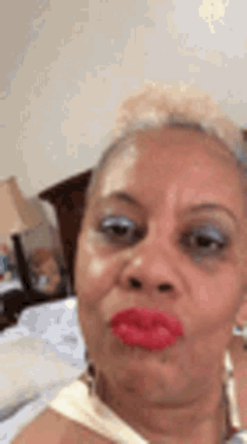 a woman with red lipstick is making a funny face while sitting on a bed .