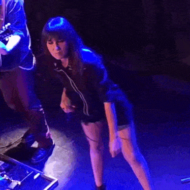a woman is standing on a stage in front of a man playing a guitar .