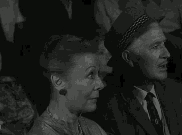 a man in a suit and tie sits next to a woman in earrings