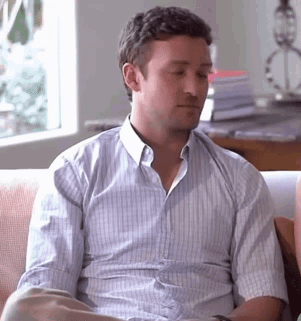 a man in a blue and white striped shirt is sitting on a couch with his eyes closed .