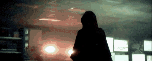 a silhouette of a person in a hooded jacket standing in a dark room .
