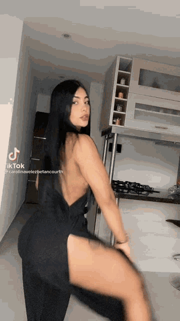 a woman in a black dress is dancing in a kitchen with a refrigerator .