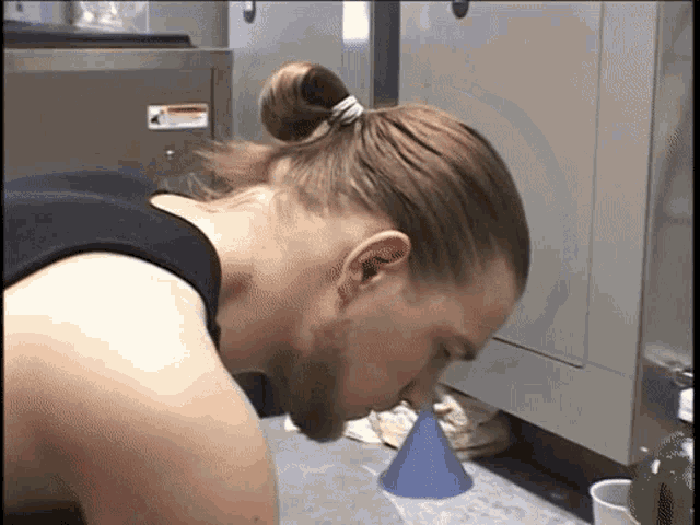 a man with a ponytail looks down at a blue cone on the floor