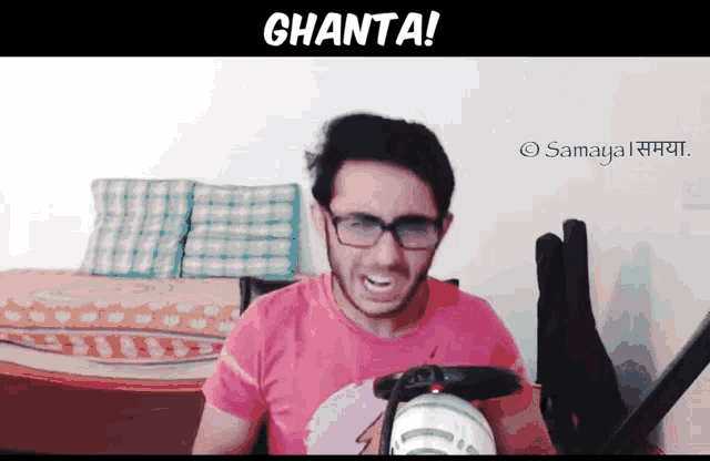 a man wearing glasses and a pink shirt is sitting in front of a wall that says ghanta